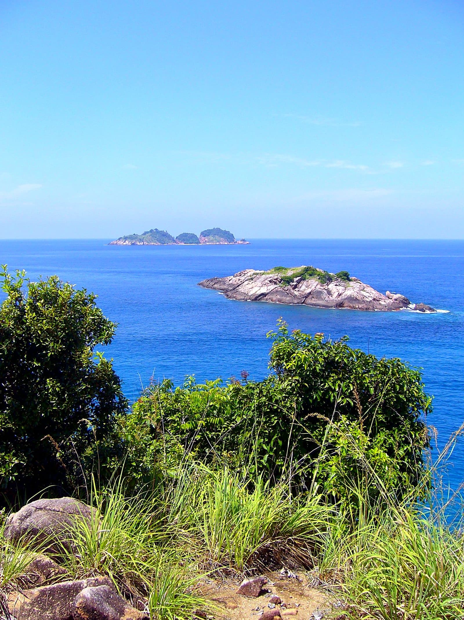 Two small rocky islets in the deep blue sea off Pulau Redang, seen from a vegetated clifftop