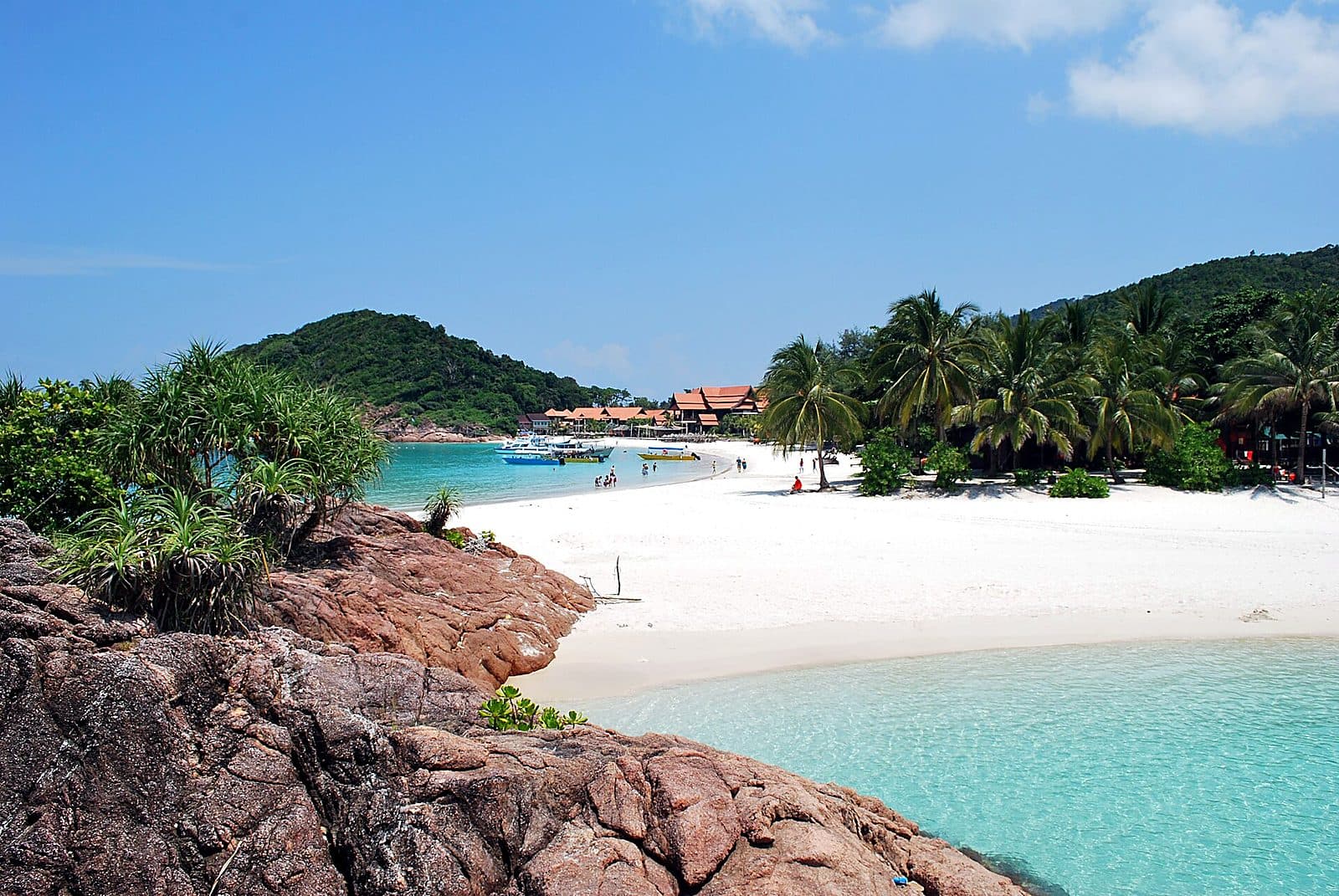 A classic Pulau Redang beach — white sand and turquoise water framed by a rocky outcrop, with resort boats offshore